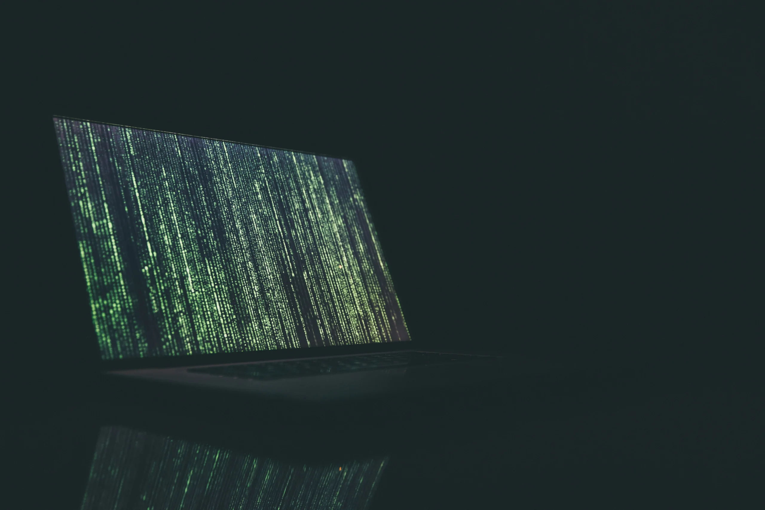 Un ordinateur portable ouvert dans le noir complet, dont l'écran affiche une cascade de lignes de code.