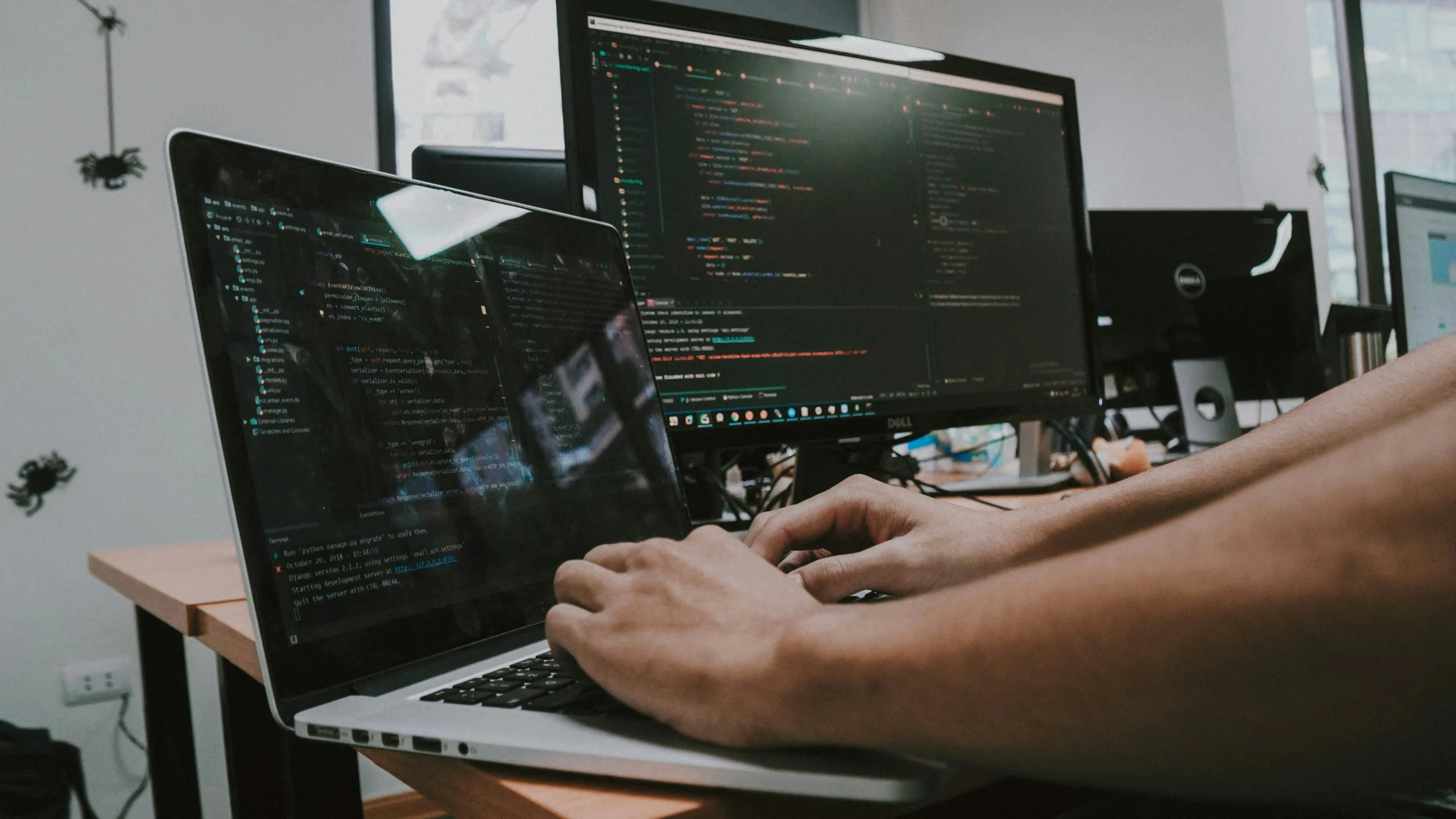 Vue rapprochée des mains d'un développeur en train de taper sur le clavier d'un ordinateur portable, connecté à un autre écran affichant du code.