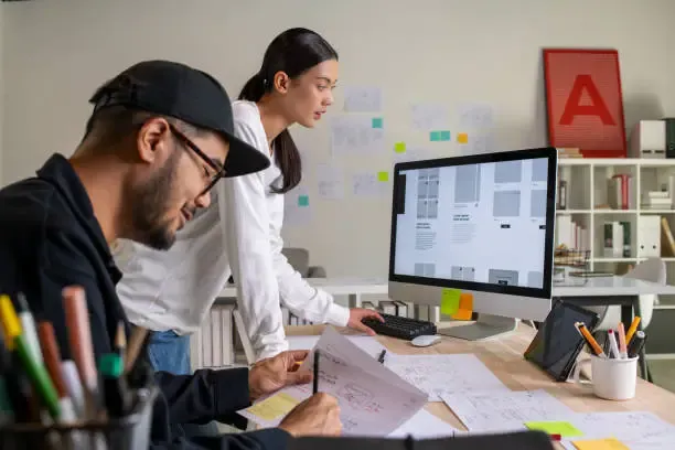 Une équipe de designers travaillant sur l'interface d'un site web sur écran d'ordinateur et maquettes papier.