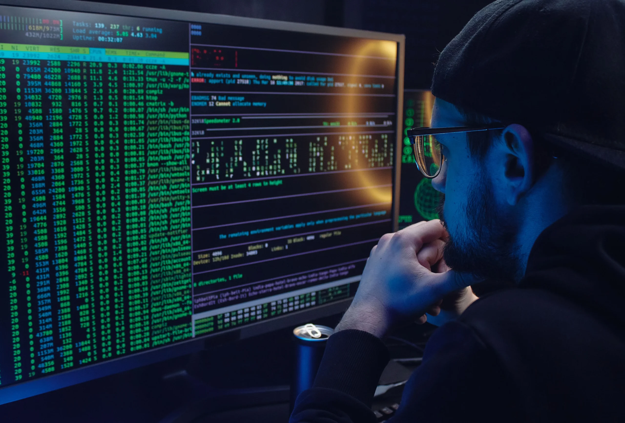 Un homme de profil, concentré sur un grand écran affichant des fenêtres de terminaux et de code.