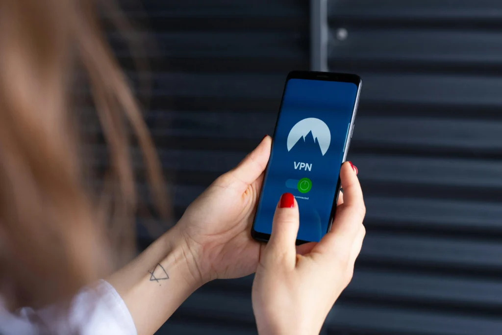 Vue de dos d'une personne tenant un smartphone qui affiche une application de réseau privé virtuel (VPN) actif.