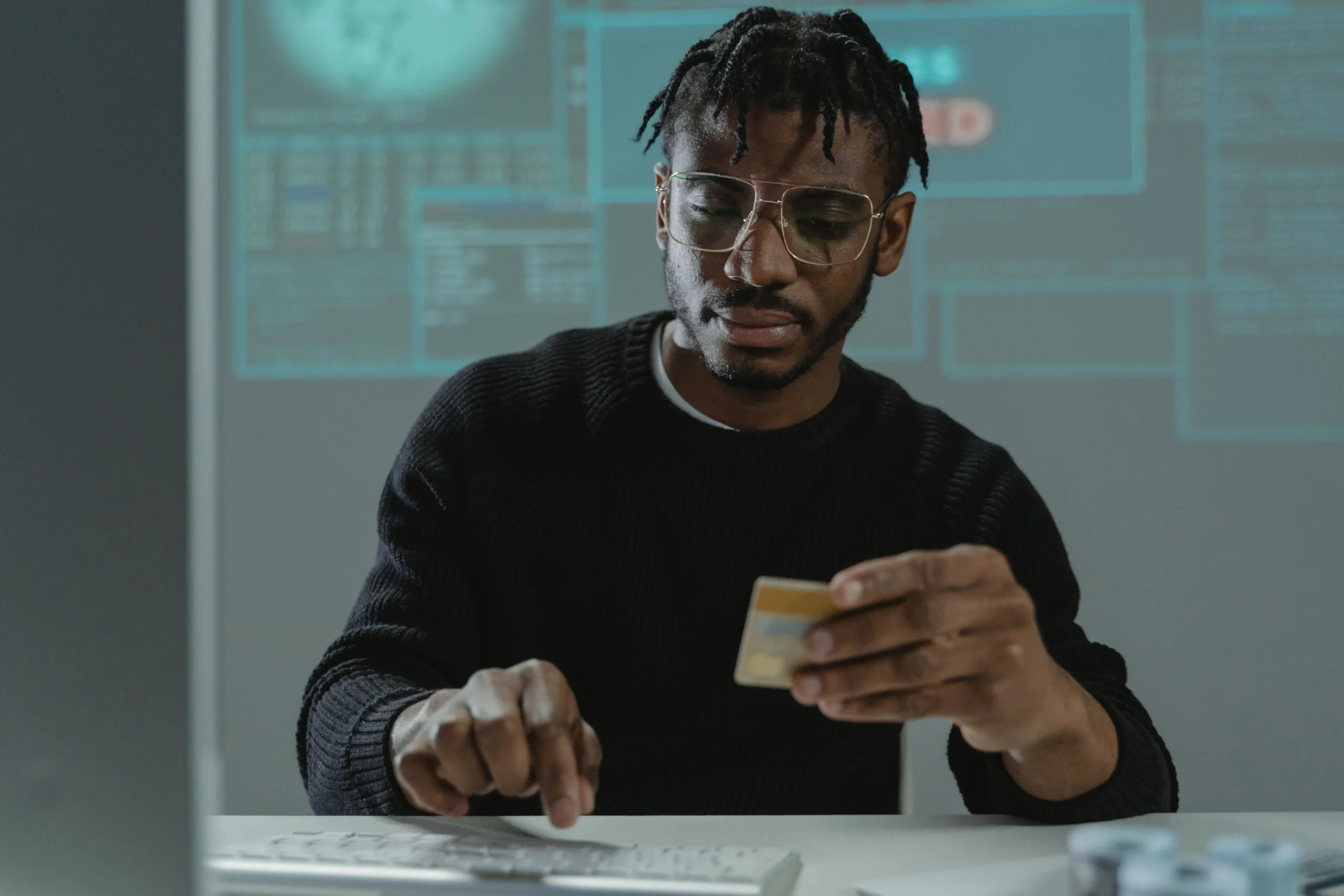 Un homme est assis à son bureau, tenant une carte bancaire d'une main et tapant sur son clavier de l'autre.