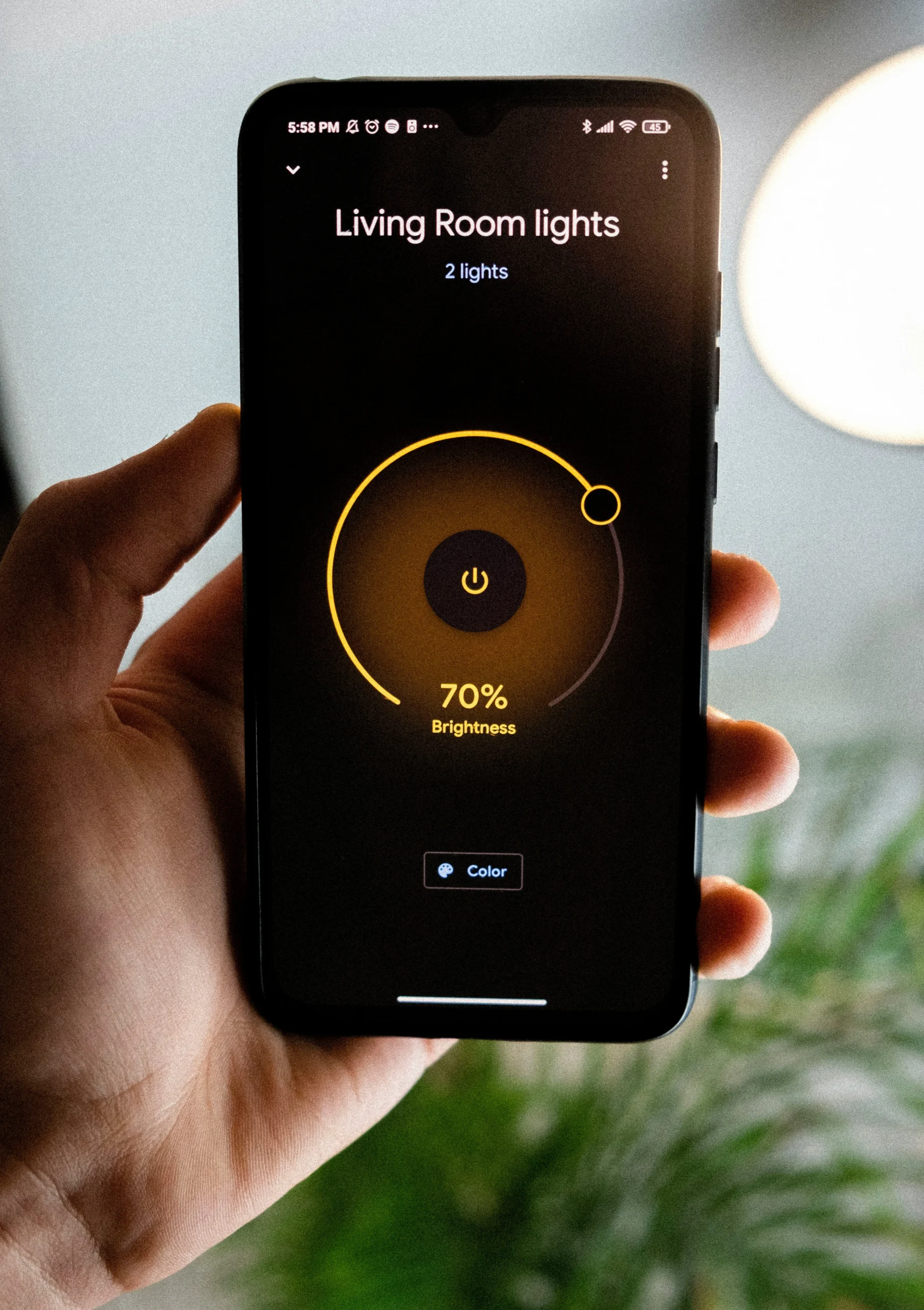 Une main tenant un smartphone qui affiche une application de contrôle de la lumière réglée à 70%.